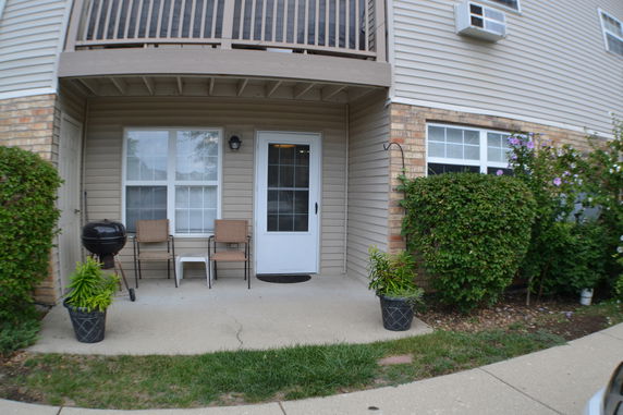 Front view of a house with a small patio, two chairs, and a door.