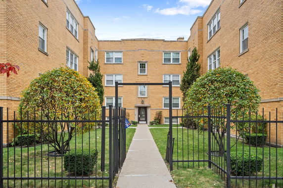Front view of a multi-story brick building with a central entrance and surrounding greenery.