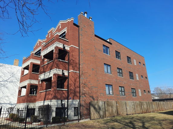 Front view of a multi-story brick building with balconies and multiple windows.