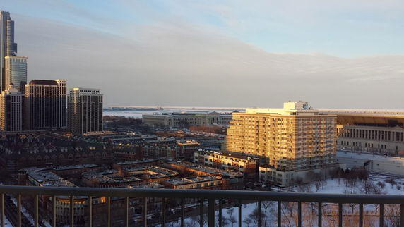 Panoramic view of a city with high-rise buildings, a large river or lake, and a snow-covered urban area.