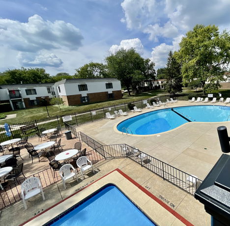 Outdoor swimming pool area with seating and nearby residential buildings.