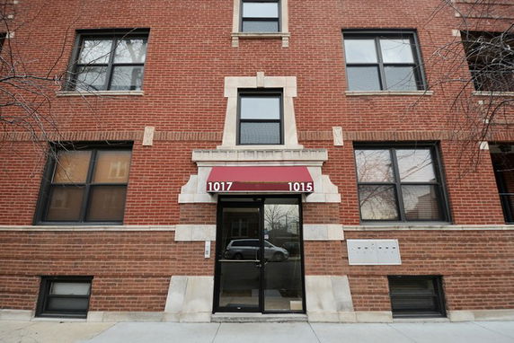 Front view of a brick apartment building with a red awning over the entrance.