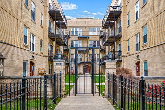 Front view of a multi-story apartment building with balconies and a gated entrance.