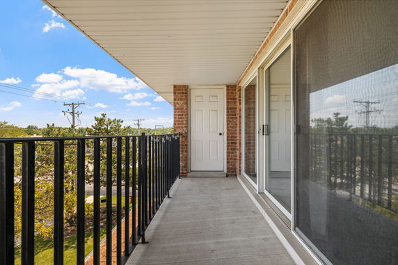 Balcony view with sliding doors and a railing overlooking trees and utility poles.