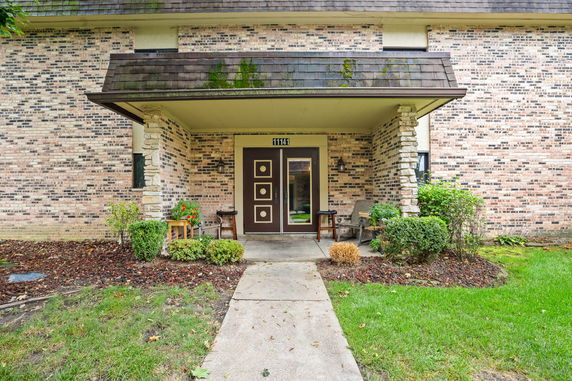 Front view of a brick house with a covered entrance and two chairs.