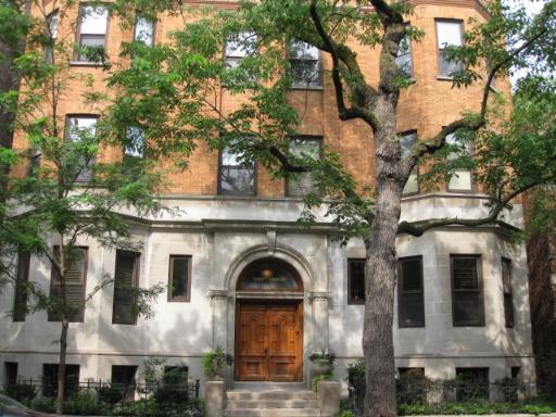 Front view of a multi-story brick building with large wooden door and arched entryway.
