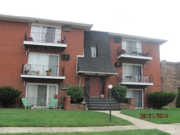 Front view of a three-story brick apartment building with balconies.