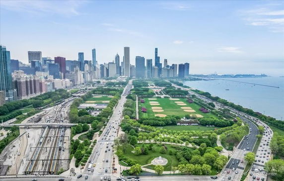 Panoramic view of a cityscape with high-rise buildings and a park along a waterfront.
