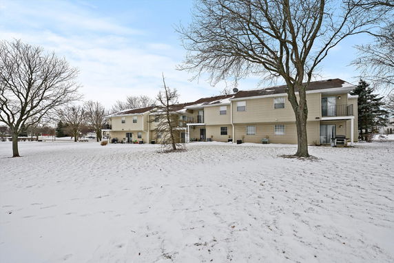 Rear view of a two-story apartment building with beige siding in a snowy landscape.