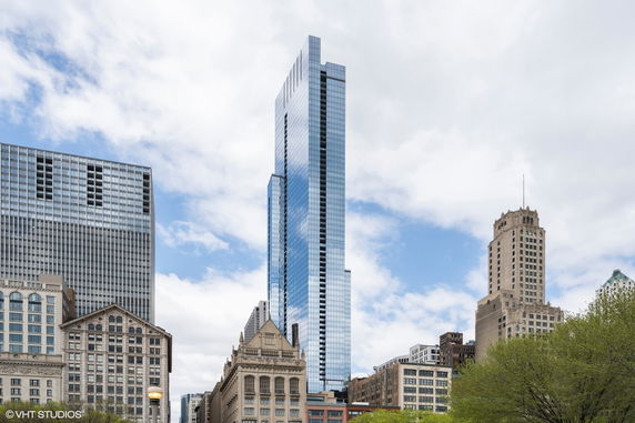 Front view of a modern skyscraper with glass facade alongside other buildings.