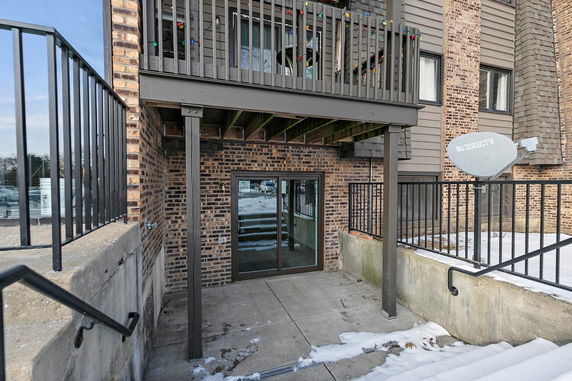 View of a building with a brick exterior and a balcony with railing above a sliding glass door entrance.