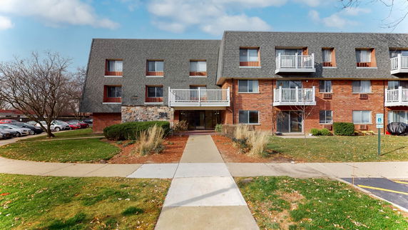 Front view of a multi-story brick apartment building with balconies and a sloped roof.
