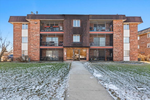 Front view of a three-story brick apartment building with balconies.