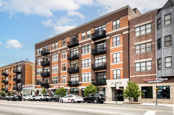 Front view of a multi-story building with balconies and storefronts on the ground level.