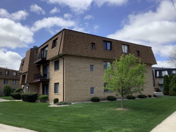 Front view of a multi-story brick building with brown sloped roofs and balconies.