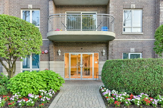 Front view of a brick apartment building with a balcony and glass entrance doors.