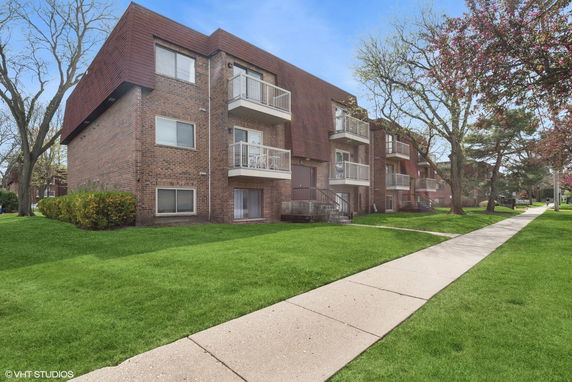 Front view of a three-story brick apartment building with balconies.