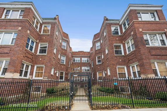 Front view of a multi-story brick residential building with a gated entrance.