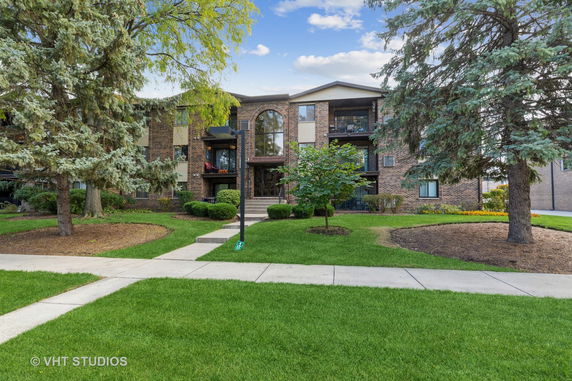 Front view of a multi-story brick residential building with balconies and landscaped surroundings.