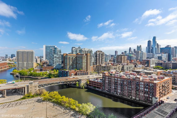 Panoramic view of a city skyline with a river and multiple high-rise buildings under a blue sky.