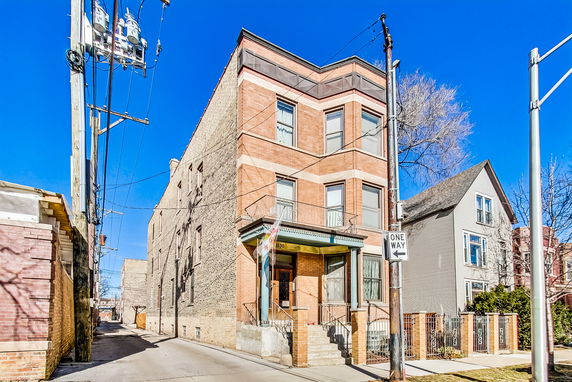 Front view of a three-story brick building on a corner lot with a one-way street sign.