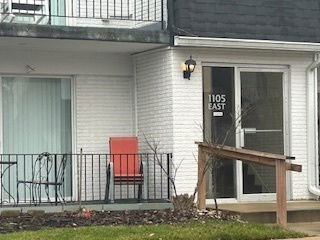 Front view of a building entrance with a balcony above and a red chair on the porch.