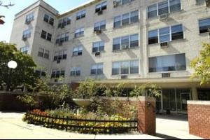 Front view of a multi-story apartment building with numerous windows and a landscaped entrance area.