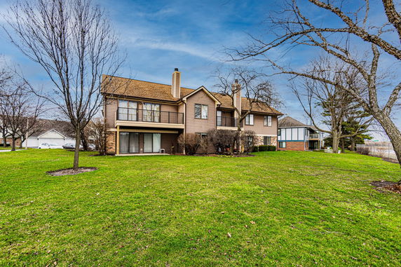 Back view of a two-story house with brown siding and chimneys.
