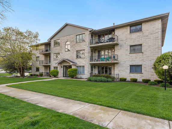Front view of a three-story brick apartment building with balconies.