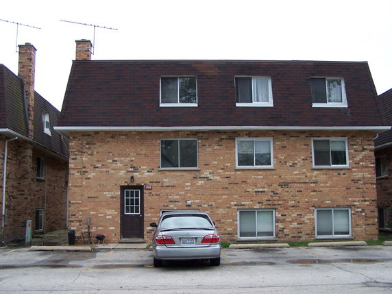 Front view of a multi-story brick building with windows and a parked car.