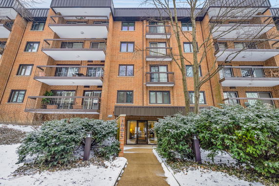 Front view of a multi-story brick apartment building with balconies and entrance pathway.
