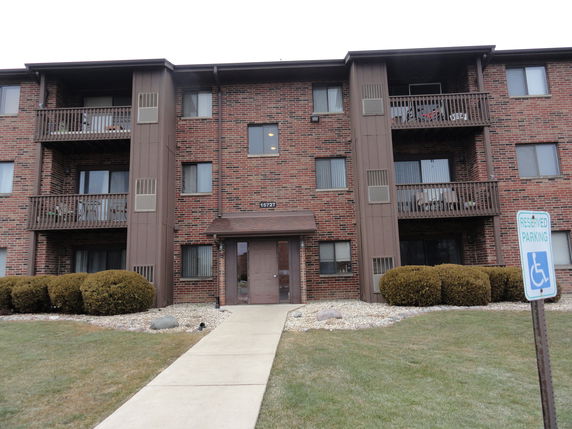 Front view of a three-story brick apartment building with balconies.