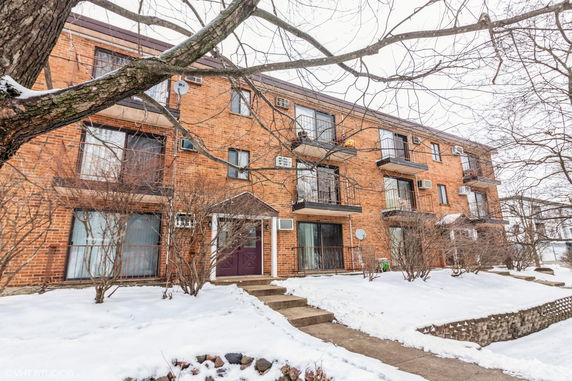 Front view of a brick apartment building with balconies and a snow-covered entrance.