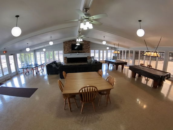 Interior view of a clubhouse with tables, chairs, sofas, and billiards tables.