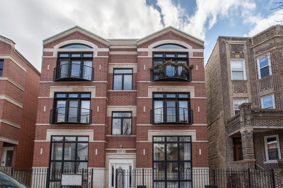 Front view of a three-story brick apartment building with balconies.