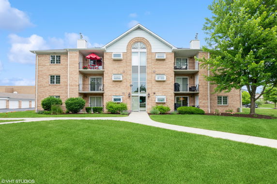 Front view of a multi-story brick apartment building with balconies and a central entrance.