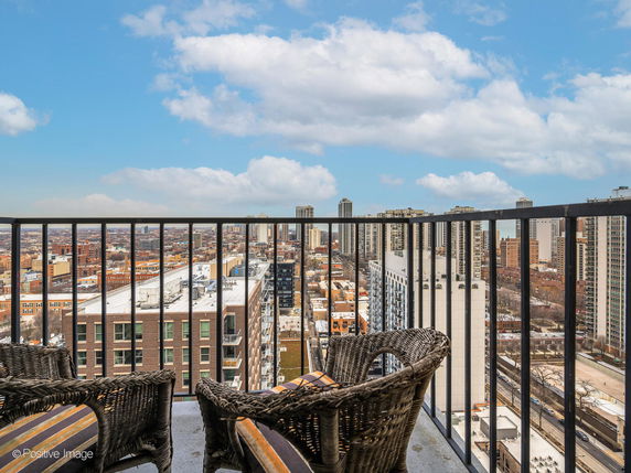 Panoramic view of a cityscape from a high-rise balcony with wicker chairs.