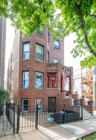 Front view of a three-story brick townhouse with stairs leading to the entrance.