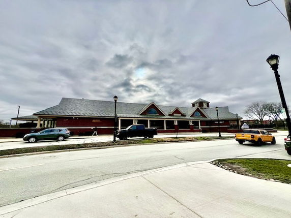 Street view of a long, single-story building with a sloped roof and several pointed gables.