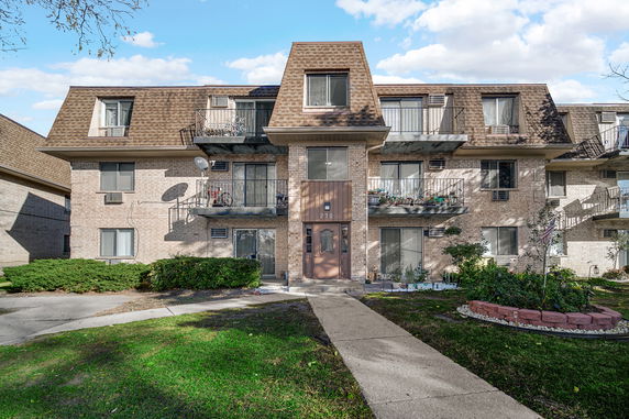 Front view of a three-story apartment building with balconies and a pathway leading to the entrance.