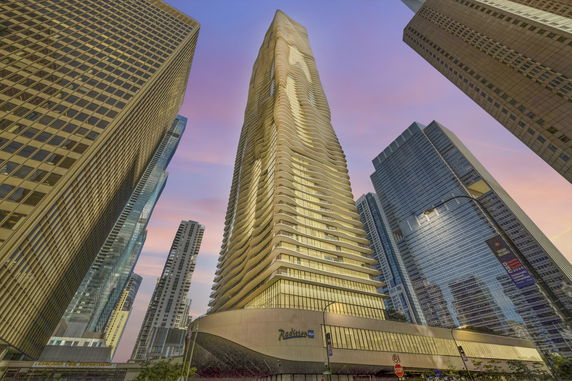Front view of a tall skyscraper with a unique wavy design, surrounded by other high-rise buildings.
