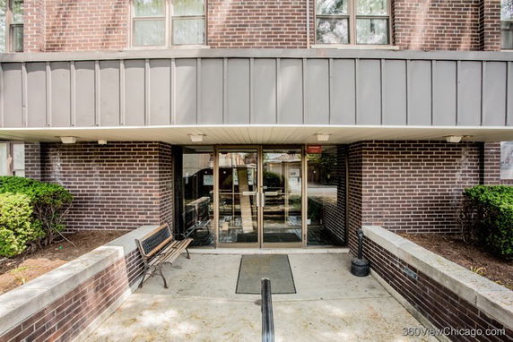 Front view of a brick building entrance with glass doors and a bench.