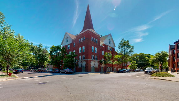 Front view of a multi-story brick building with a pointed spire.