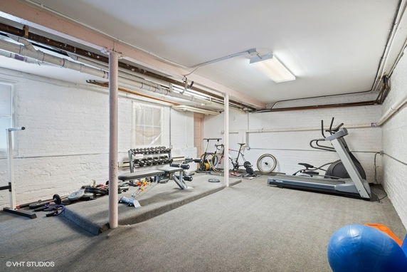 Indoor gym area with exercise equipment in a room with exposed pipes and carpeted floor.