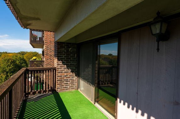 View from a balcony with a brick exterior and glass sliding door, overlooking treetops.