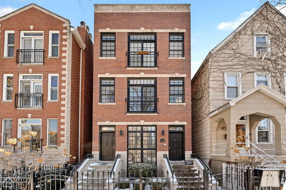 Front view of a three-story brick building with black doors and metal railings.