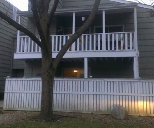 Front view of a two-story house with a balcony and a white fence.