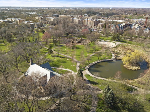 Panoramic view of a park area with trees, pathways, and a small lake.