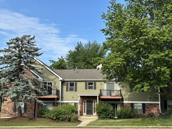 Front view of a two-story residential building with balconies and a mixed brick and wood exterior.