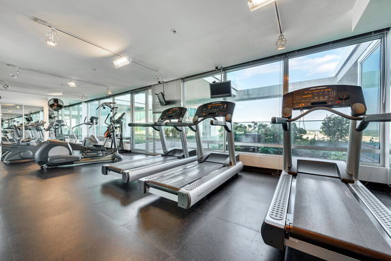 Indoor gym with treadmills and exercise equipment facing large windows.